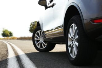 Detailný pohľad na auto na ceste, zdôrazňujúci kolesá a asfalt.
