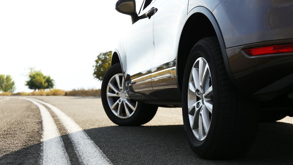 Detailný pohľad na auto na ceste, zdôrazňujúci kolesá a asfalt.