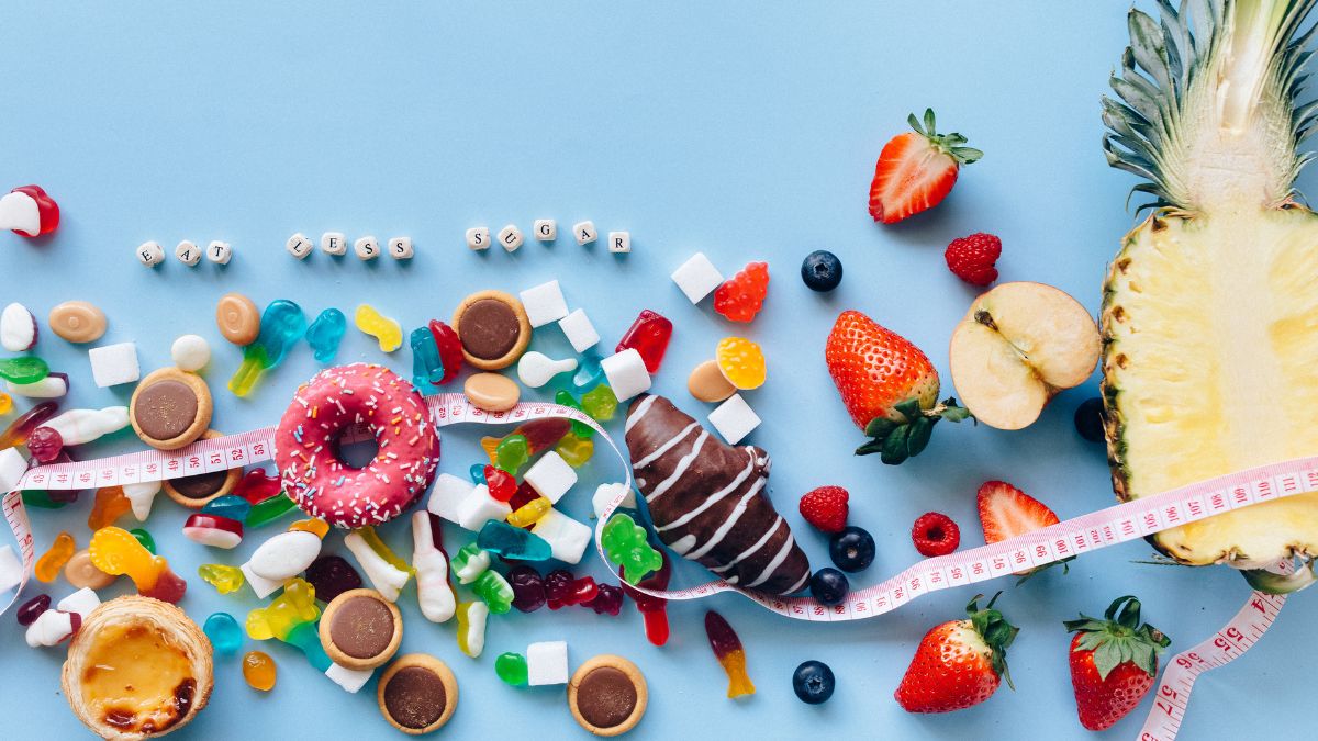 Rôzne sladkosti a ovocie na modrom pozadí, s meracou páskou a nápisom 'eat less sugar'.