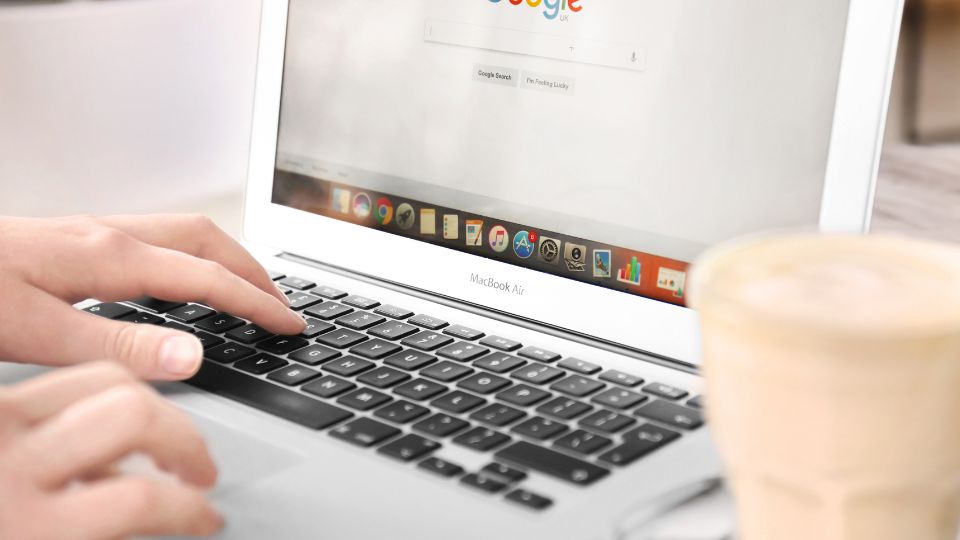 Ruka píše na klávesnici MacBooku s otvoreným Google vyhľadávačom.