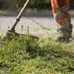 Záber na motorovú kosu v akcii, kosí trávu a burinu.
