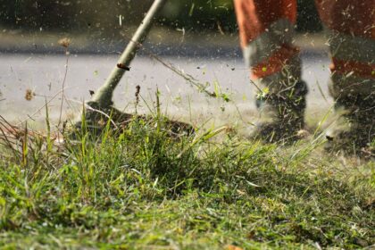 Záber na motorovú kosu v akcii, kosí trávu a burinu.