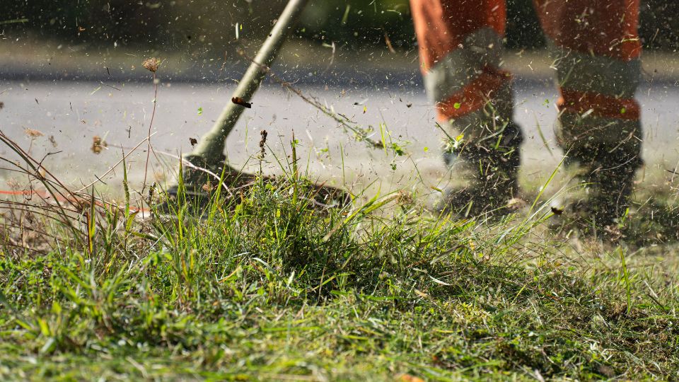 Záber na motorovú kosu v akcii, kosí trávu a burinu.
