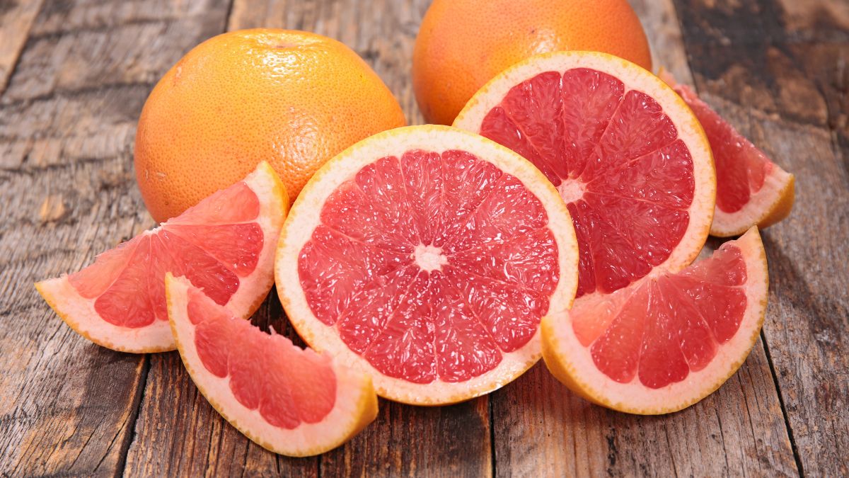 Čerstvý grapefruit rozkrojený na plátky, s celými kusmi na drevenom stole.