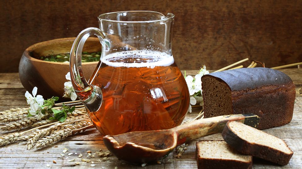Sklenená karafa s kvasom, vedľa chlieb a prírodné ingrediencie.