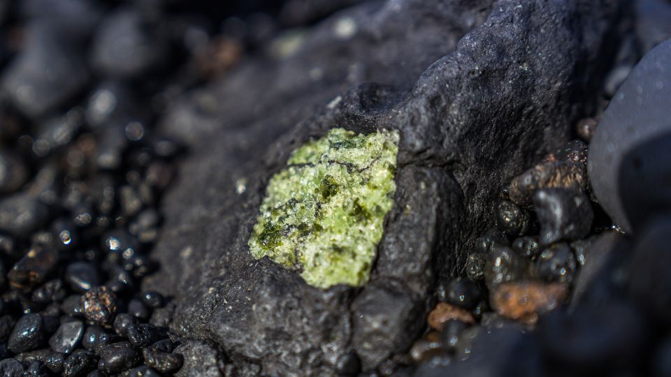 Lávový kameň s jasne zeleným minerálom na čiernej skalnej ploche.