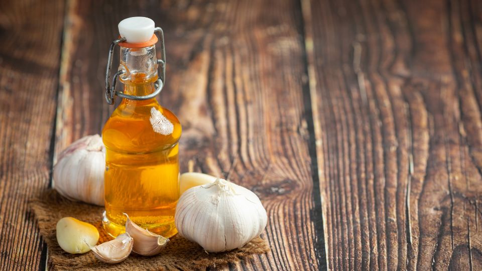 Fľaša maslového oleja vedľa strúčikov cesnaku na drevenom stole.