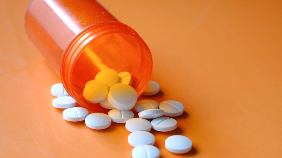 Rozliate biele tablety na oranžovom pozadí, symbolizujúce antibiotiká.