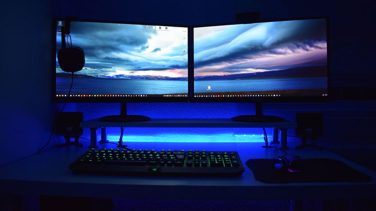Dva LCD monitory na stole s klávesnicou a myšou, osvetlené modrým svetlom.