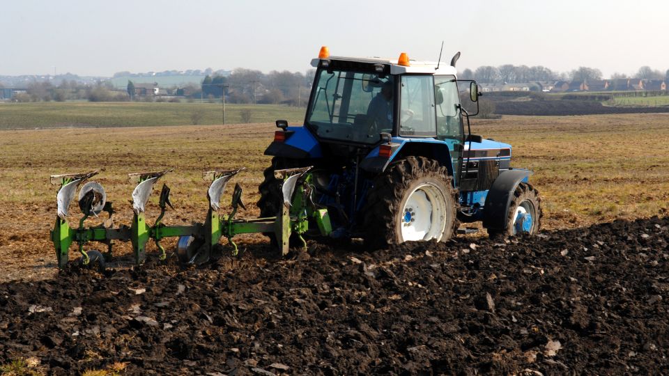 Traktor s obracecím pluhem pracuje na ornej pôde v poľnohospodárskom prostredí.