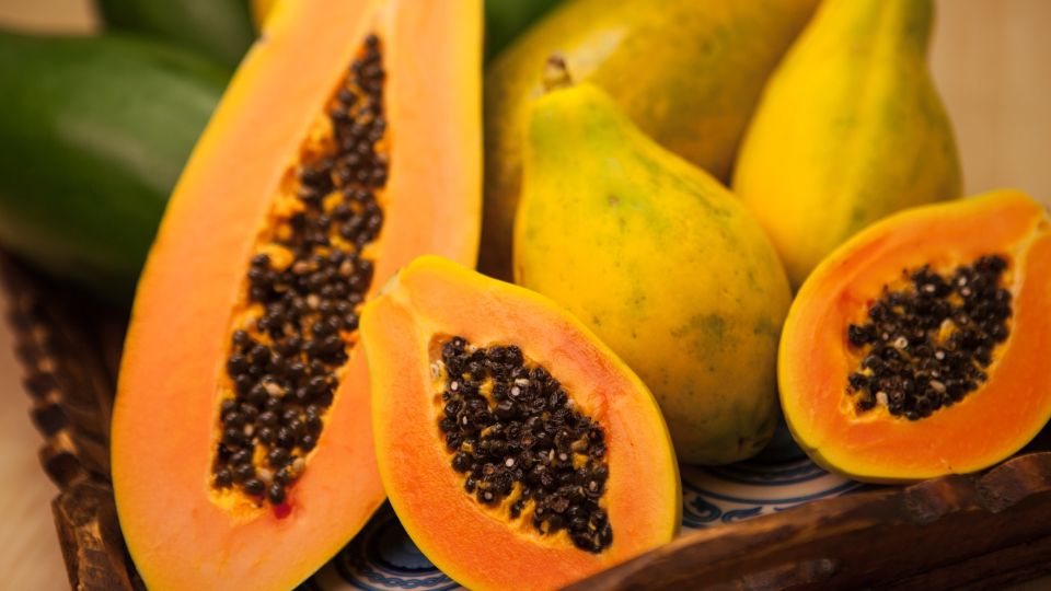 Zrelé papáje s jasne oranžovou dužinou a čiernymi semienkami na drevenom podnose.