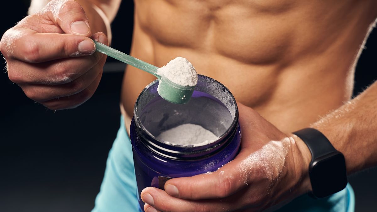 Muž drží odmerku s proteínovým práškom nad otvorenou nádobou.