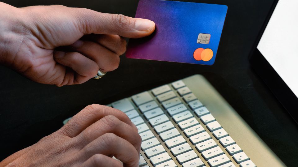 Ruka drží platobnú kartu pred klávesnicou počítača, symbolizujúca online platby.