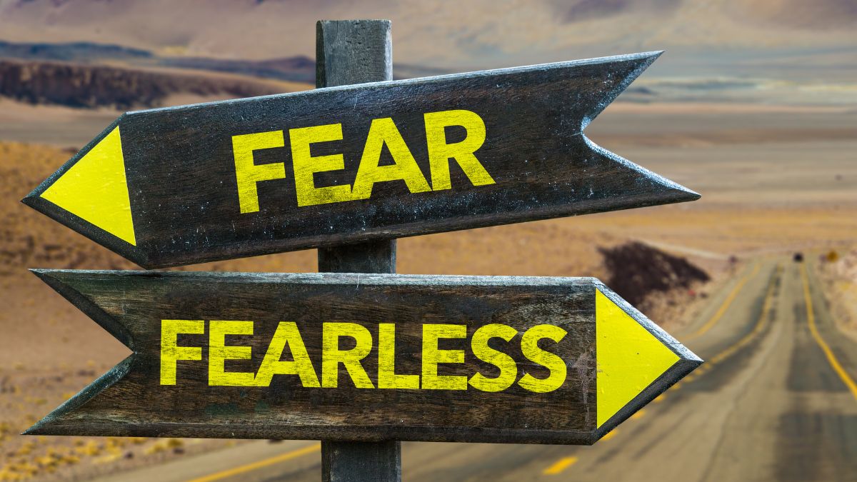 Drevené smerovníky s nápismi 'FEAR' a 'FEARLESS' ukazujú na dve rôzne cesty v pustej krajine.