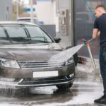 Mladý muž umýva čierne auto na samoobslužnej autoumyvárni.