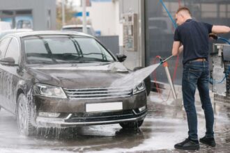 Mladý muž umýva čierne auto na samoobslužnej autoumyvárni.