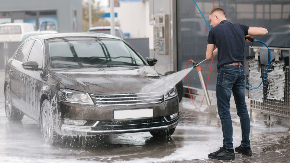 Mladý muž umýva čierne auto na samoobslužnej autoumyvárni.