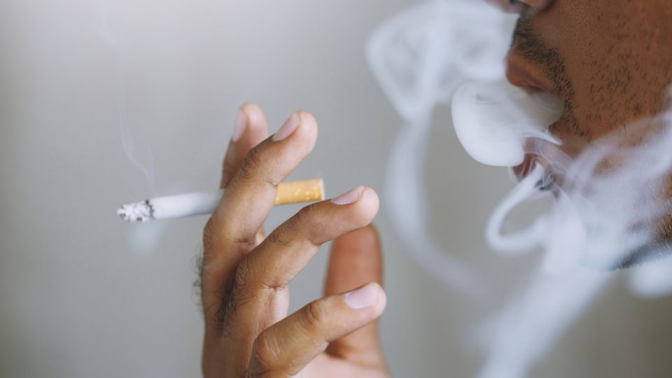 Muž fajčí cigaretu, dym sa vznáša okolo jeho tváre.