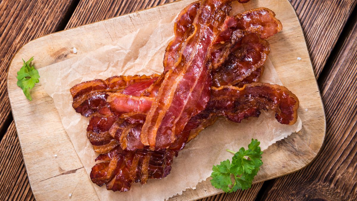 Chrumkavá slanina na drevenej doske s bylinkou vedľa.