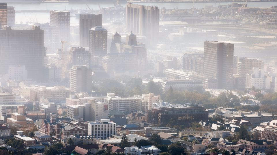 Mestská panoráma zahalená v smogu, s rozmazanými budovami a znečisteným ovzduším.