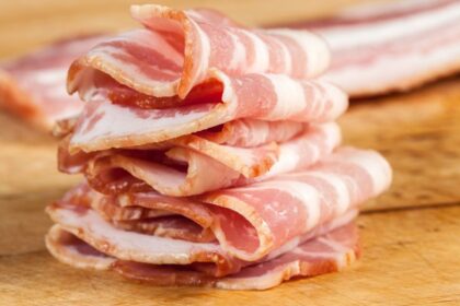 Usporiadané plátky slaniny na drevenej doske, s viditeľnou mastnou textúrou.