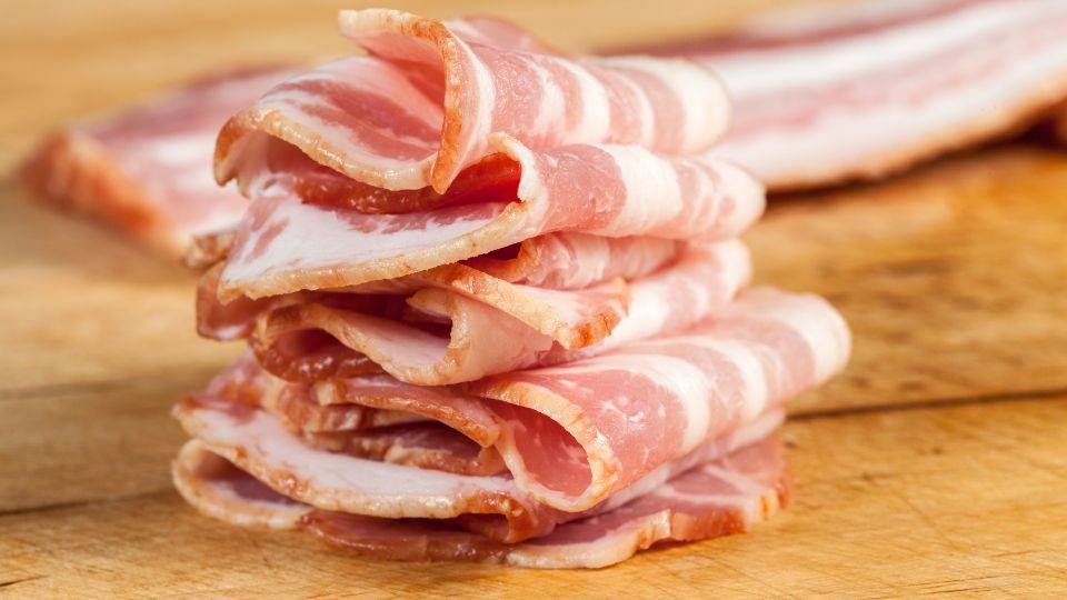 Usporiadané plátky slaniny na drevenej doske, s viditeľnou mastnou textúrou.