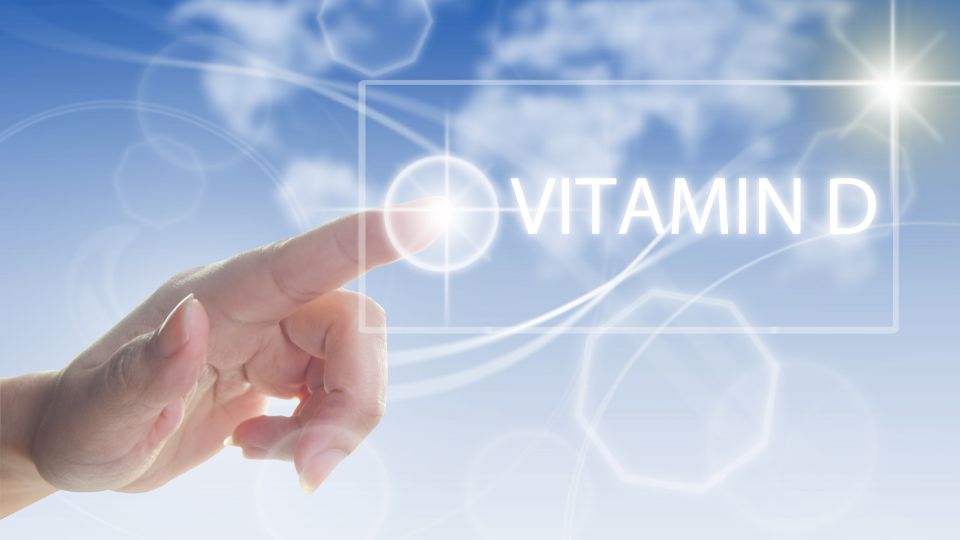 Ruka ukazujúca na nápis Vitamín D na modrom pozadí.