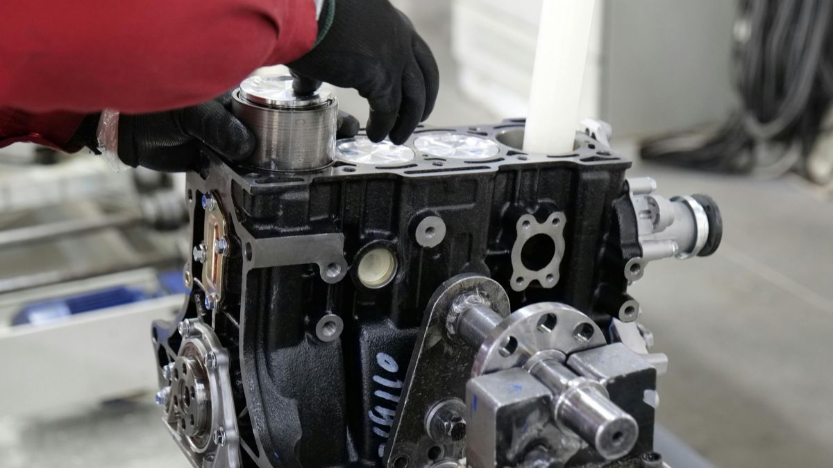 Mechanik montuje súčiastku na motor, ukazujúc proces zostavovania.