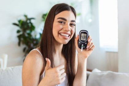 Mladá žena sa usmieva a ukazuje glukomer s hodnotou 4.8.