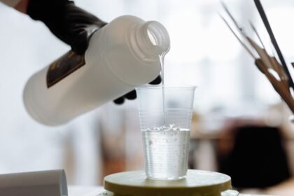 Ruka s čiernou rukavicou nalieva cukrovú pastu do plastového pohára.