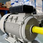 Detailný pohľad na elektromotor s žltým hriadeľom v priemyselnom prostredí.
