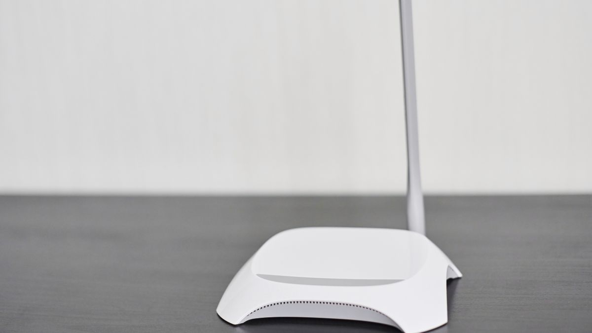Biely router na čiernom stole, symbolizujúci sieťové pripojenie.