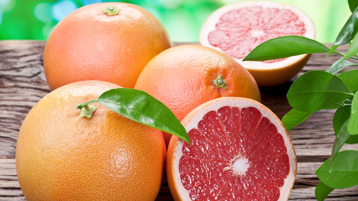 Na drevenom stole sú zobrazené celé a rozkrojené grapefruitové plody s listami.