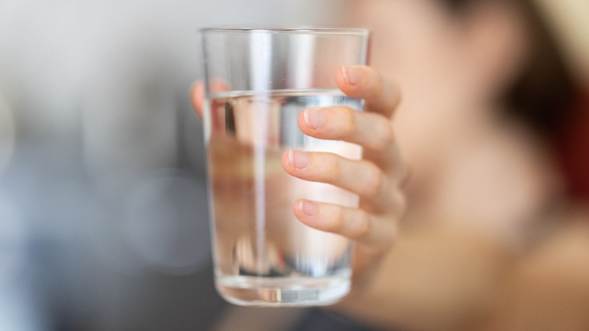 Žena drží pohár čistej vody, symbolizujúci hydratáciu a zdravie.