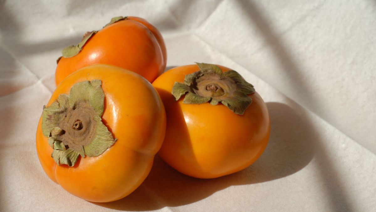 Tri zrelé kaki ovocie s jasne oranžovou farbou a zelenými listami.