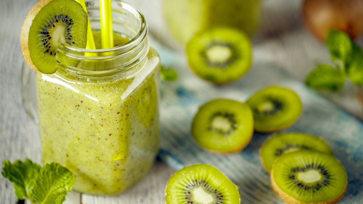Zelený smoothie s kivi a mätou v sklenenej nádobe, okolo sú plátky kivi.