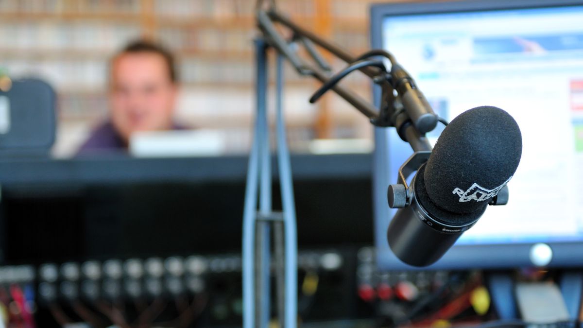 Mikrofón v rádiovom štúdiu, s pozadím technológie a pracovníka.