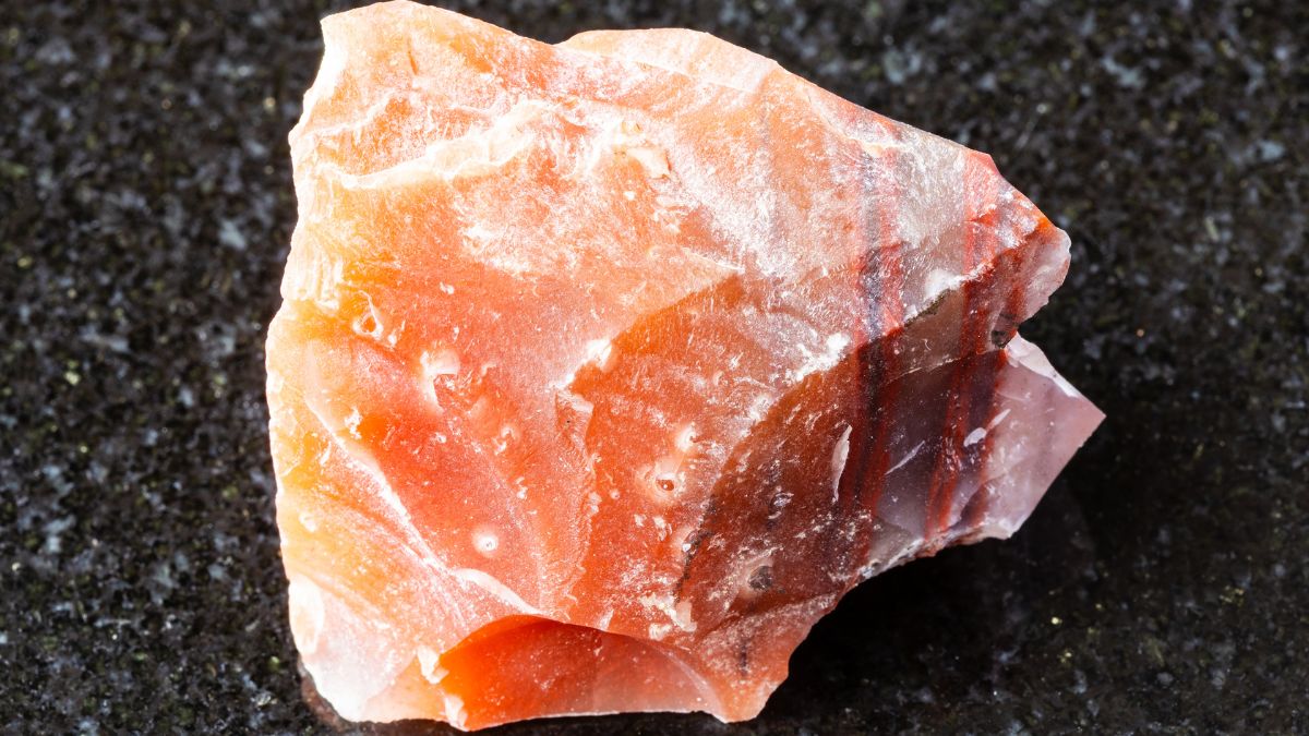Mokait minerál s teplými odtieňmi červenej a oranžovej farby na čiernom pozadí.