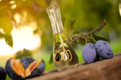 Fľaša pálenky vedľa zrelých sliviek na drevenej doske.