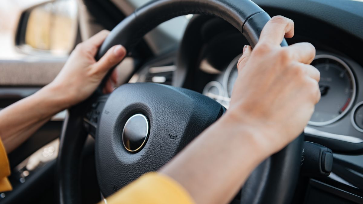 Ruka drží volant moderného automobilu, symbolizujúca kontrolu a riadenie.