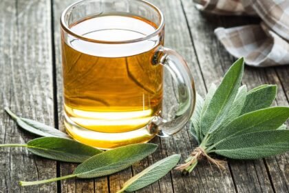 Šalviový čaj v sklenenej šálke s čerstvými šalviovými listami na drevenom stole.