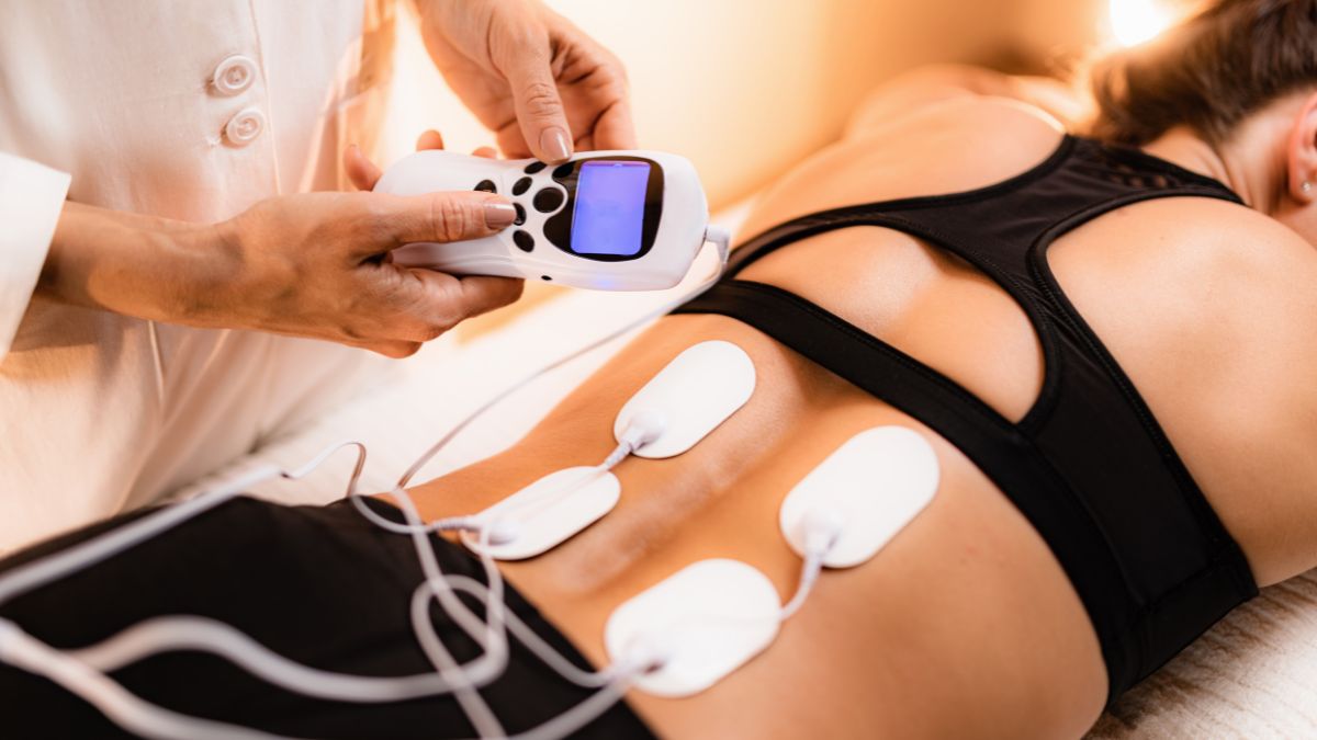 Žena podstupuje TENS terapiu s elektródami na chrbte, ktoré zmierňujú bolesť.