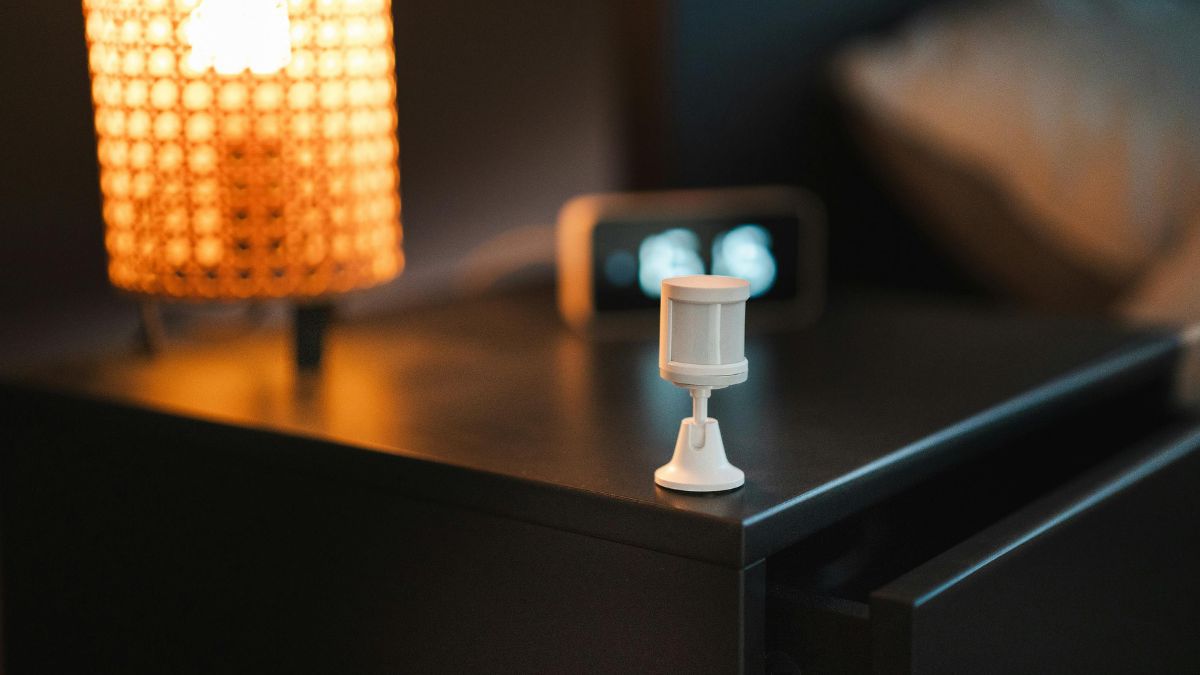 Biely teplotný senzor umiestnený na nočnom stolíku vedľa lampy.