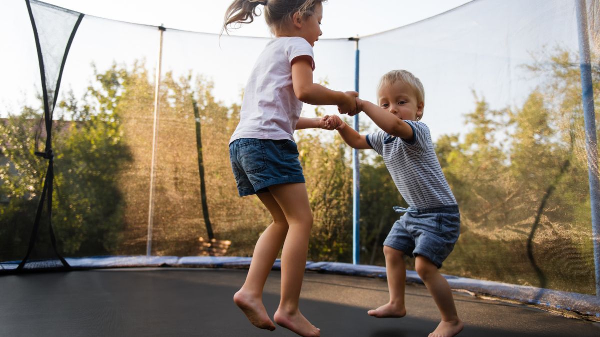 Dve deti skáču na trampolíne, radosť a pohyb v prírode.