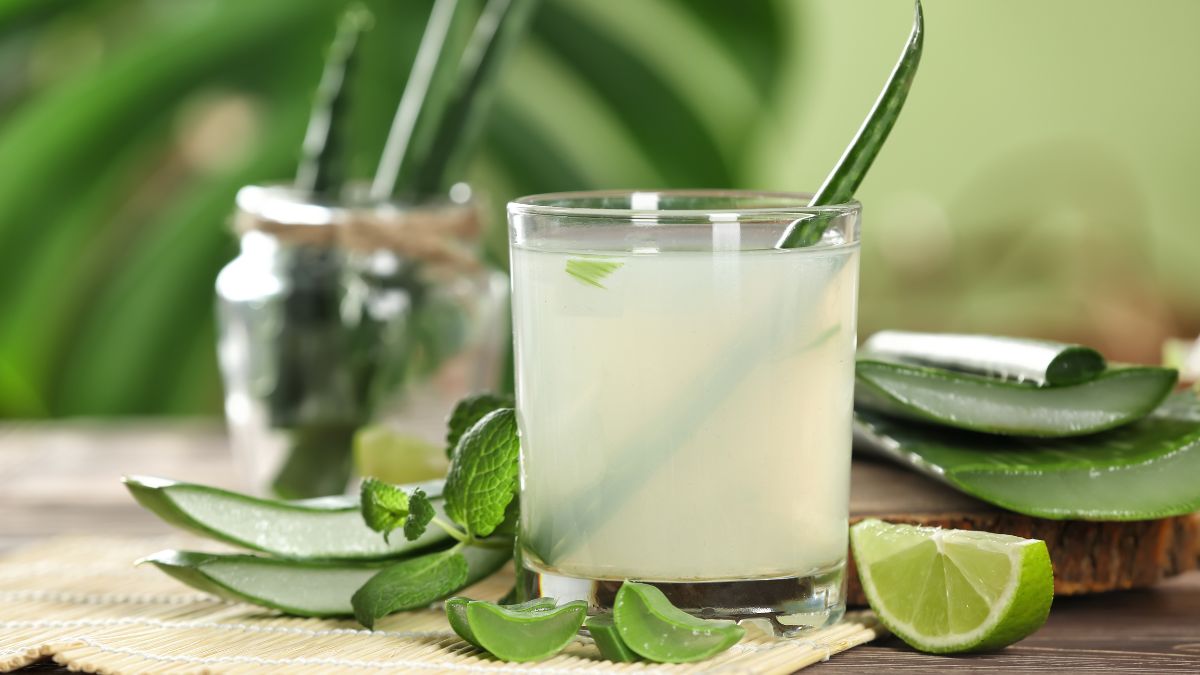 Sklenený pohár s aloe vera gélovým nápojom a plátkom limetky na drevenej doske.