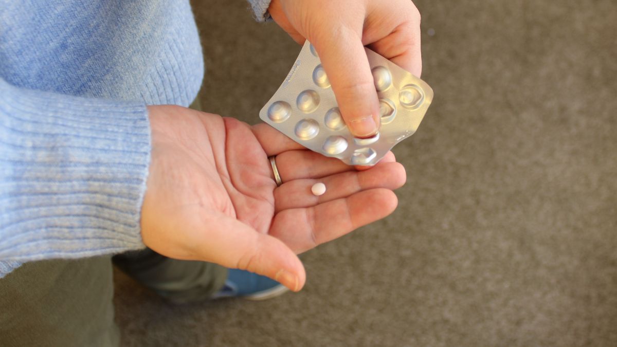 Ruka drží blistr s antipsychotickými tabletami a jednu tabletu v dlani.