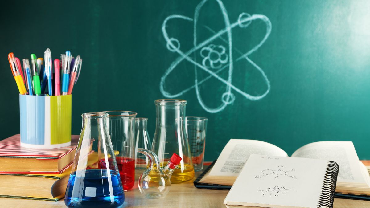 Laboratórne sklo s rôznymi chemikáliami a učebnicami na stole.
