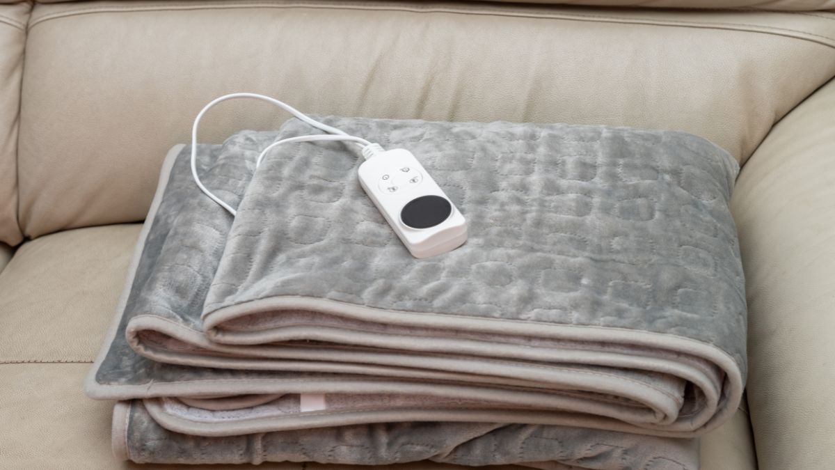 Sivá elektrická prikrývka s ovládačom na svetlom béžovom gauči.