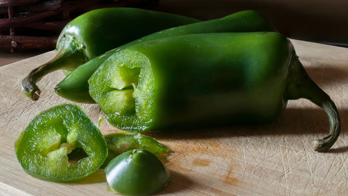 Na drevenej doske sú čerstvé jalapeño papričky, niektoré nakrájané na plátky.