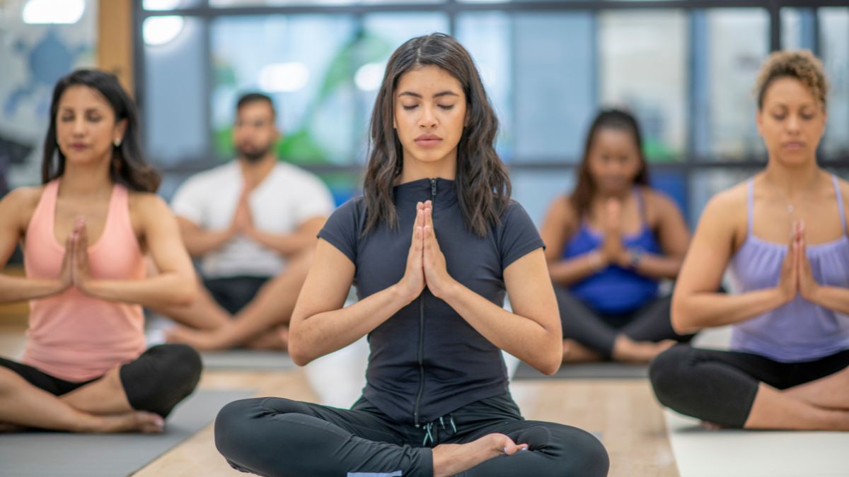 Skupina ľudí cvičí jogu v štúdiu, sústredení a v meditácii.